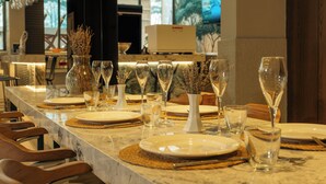 Un ambiente de restaurante con una larga mesa de comedor, varias copas de vino y un florero con flores secas.