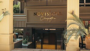 Exterior del Novishotel con doble entrada, palmeras y una vista despejada del interior.