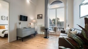 A modern living room with a sofa, a coffee table, and a TV mounted on the wall. There is a window with a view of the outdoors. - 7Florence  (Florence)