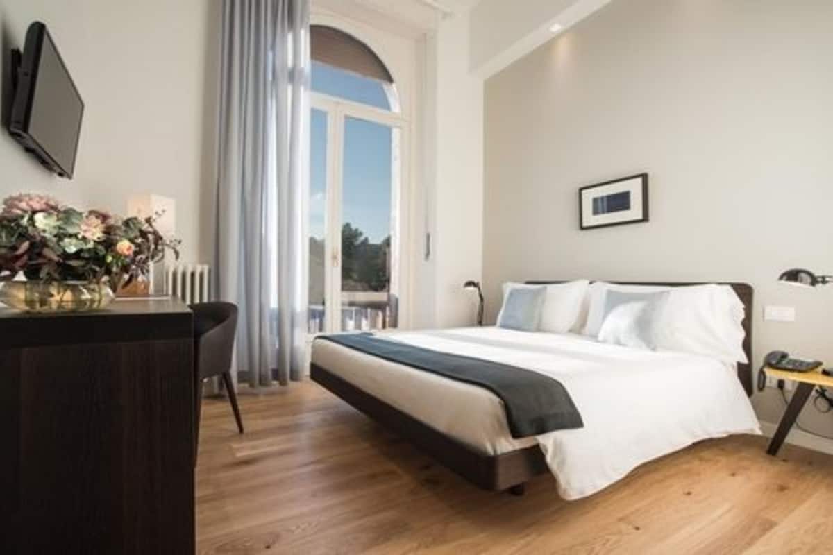 A modern hotel room with a large bed, a desk, and a view of the outdoors.