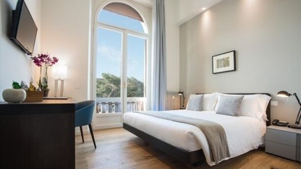 A modern bedroom with a large bed, a desk, and a window with a view of trees. - 7Florence  (Florence)