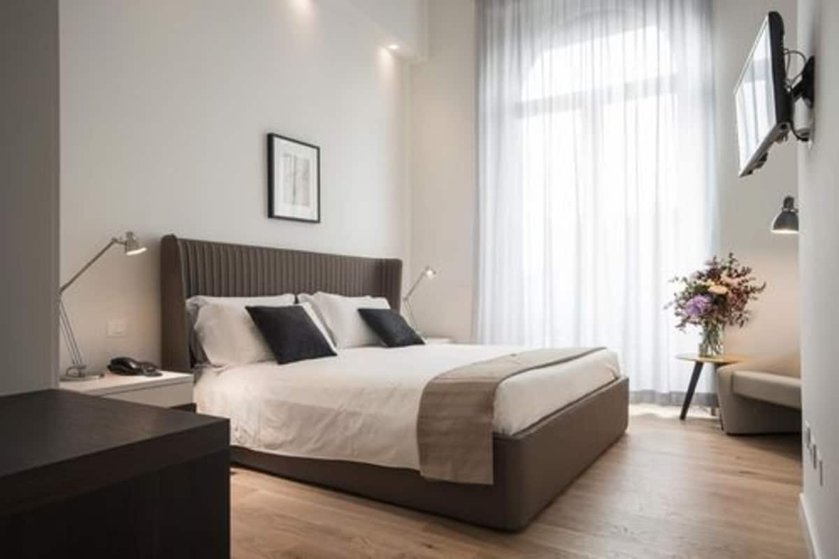 A modern bedroom with a bed, bedside tables, a desk, a chair, and a window with curtains.