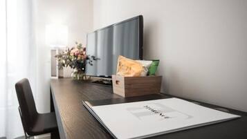 A hotel room with a wooden desk, a television, a vase with flowers, and a bag of snacks.