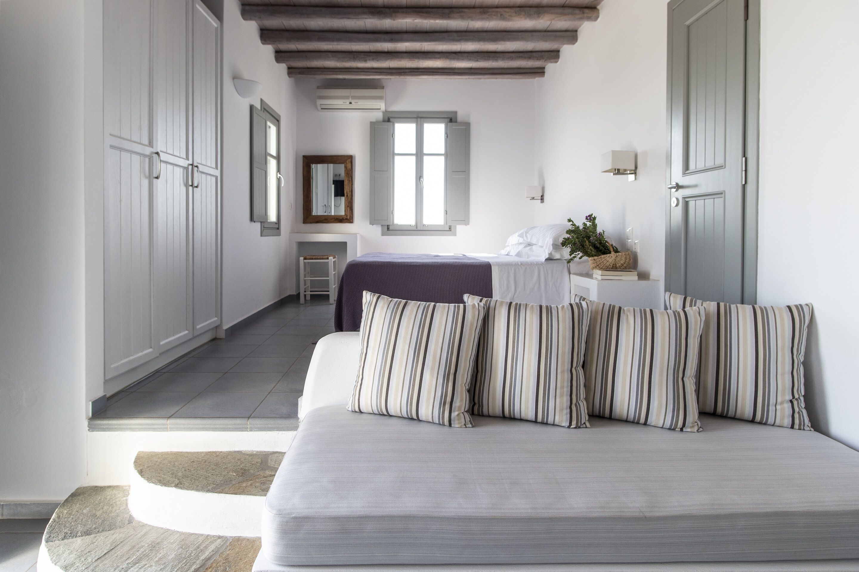 Une chambre à coucher moderne avec un grand lit, une armoire, une fenêtre et une petite table sur laquelle est posée une plante.