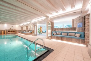 An indoor swimming pool with a wooden ceiling, stone walls, and a blue sofa with cushions. - Dein Engel (Oberstaufen)