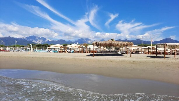 A beach with umbrellas and beach chairs, a clear sky, and mountains in the background. - Art Hotel Pietrasanta (Pietrasanta)