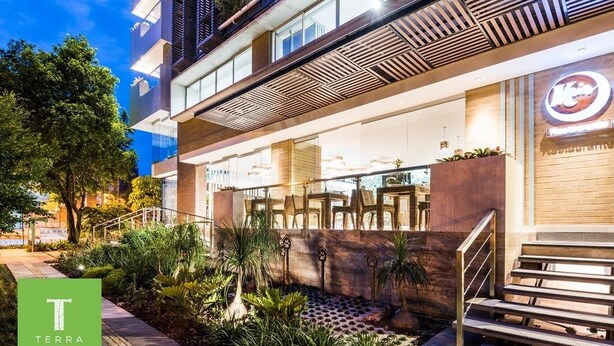 L’extérieur d’un hôtel moderne, avec une enseigne indiquant la présence d’un restaurant, des tables à l’extérieur et un jardin aménagé.