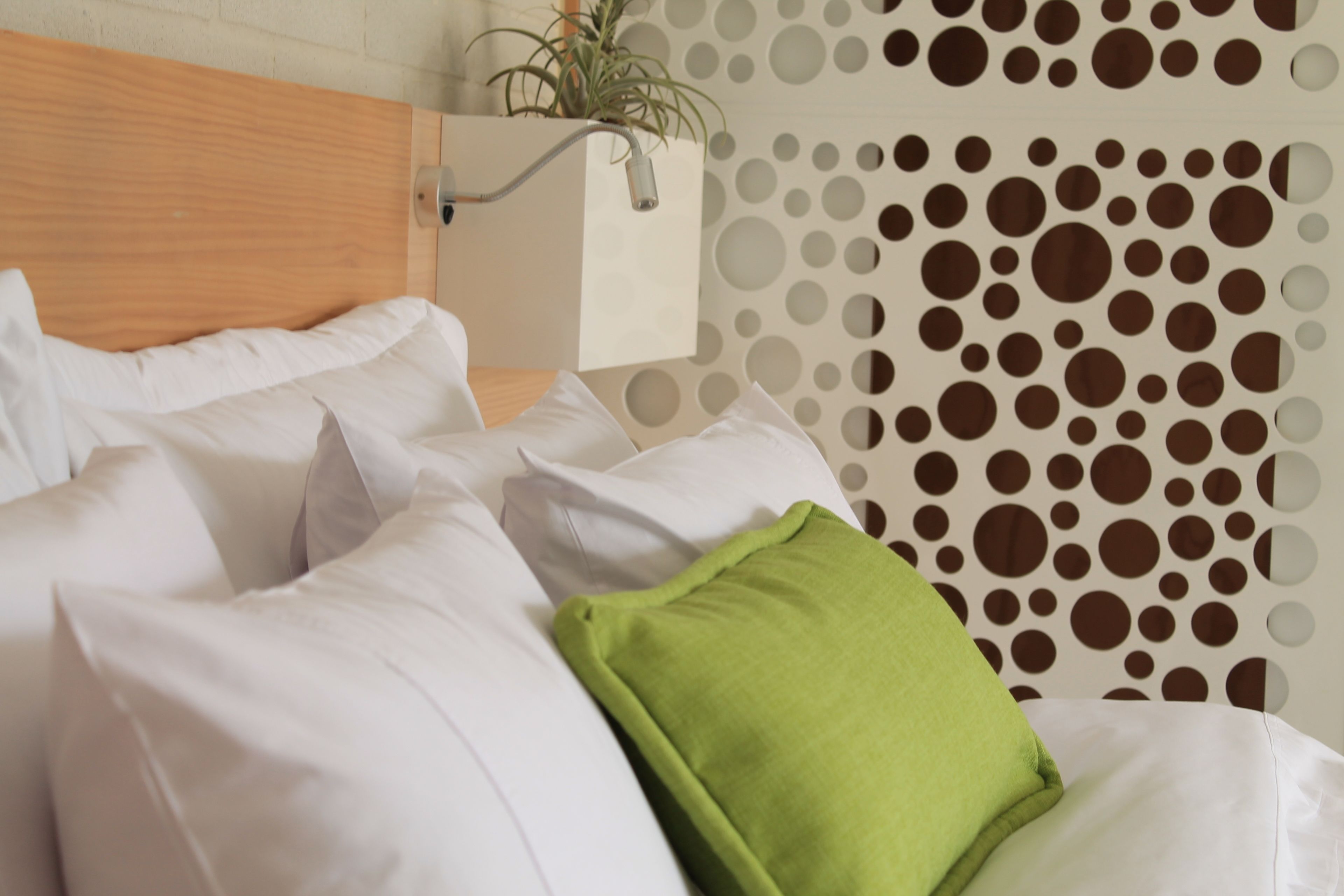 A neatly made bed with white bedding and a single green pillow.