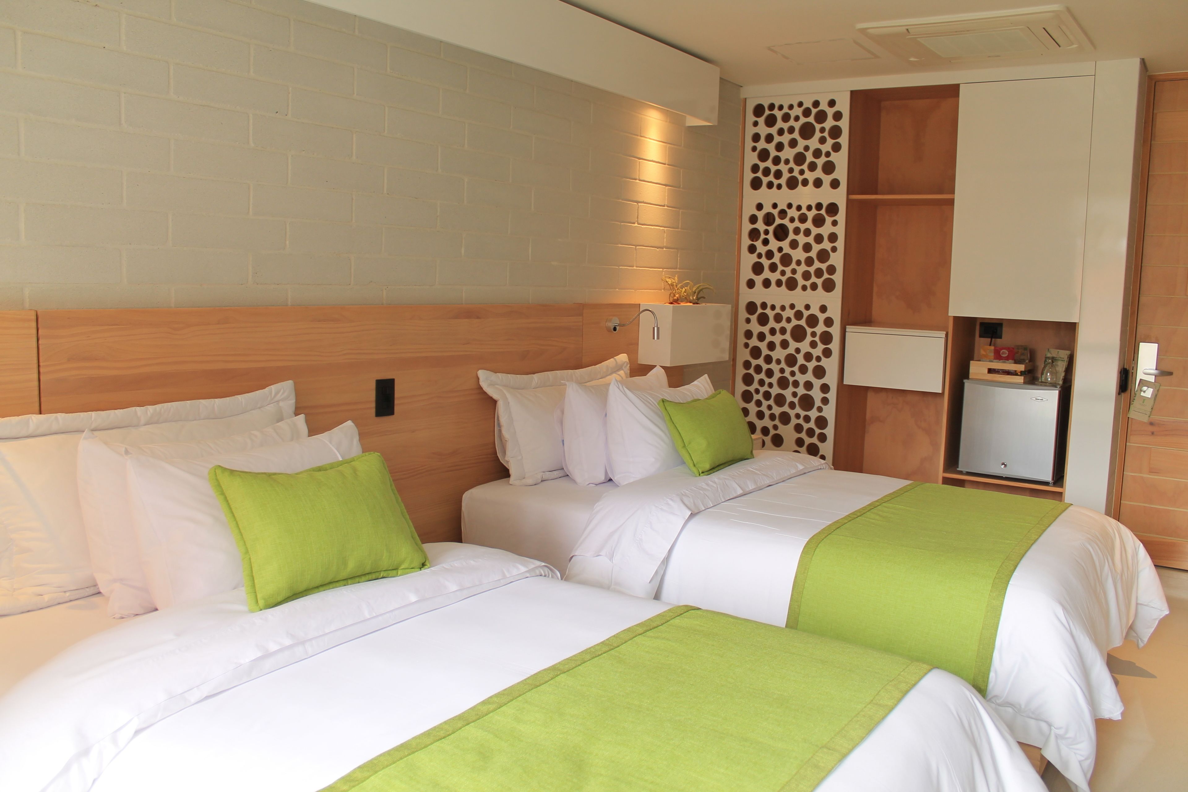 A hotel room with two beds, a brick wall, a wooden headboard, a wall-mounted light, and a storage unit with a decorative panel.