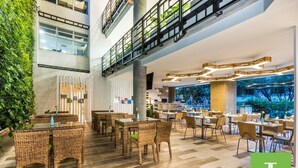 Un hall d’hôtel moderne, doté de meubles en osier, d’une rambarde en verre et offrant une vue sur l’extérieur.