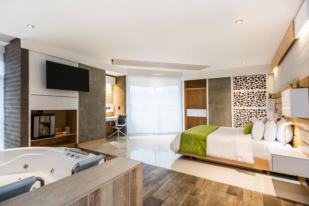 Een moderne hotelkamer met een groot bed, een bureau, een stoel, een televisie, een minibar en een badkamer met een bad.