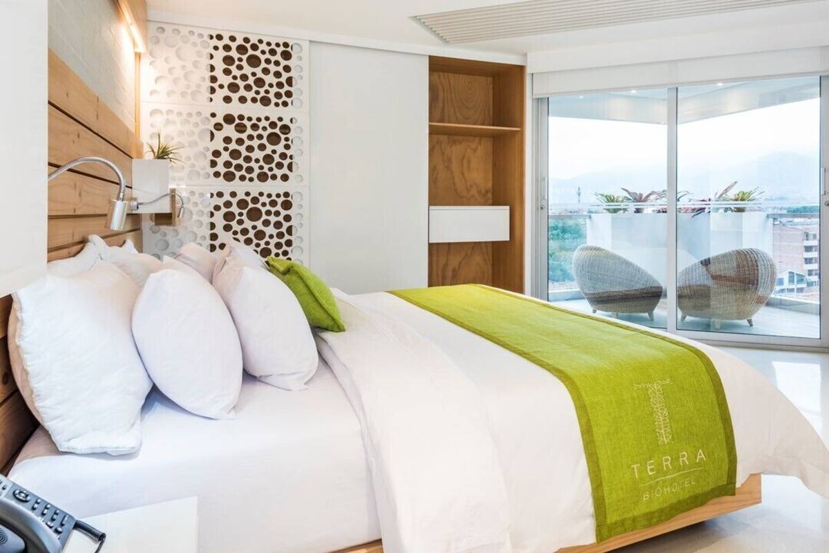 Een moderne hotelkamer met een bed, een televisie, een balkon met zitplaatsen en uitzicht op de stad.