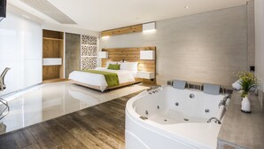Une chambre d’hôtel moderne dotée d’une grande baignoire, d’un lit avec une tête de lit en bois et d’un téléviseur fixé au mur.