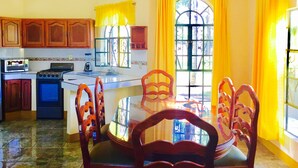 A kitchen with wooden cabinets, a stove, a sink, and a dining table with chairs. - Guamúchil Parque Acuático & Cabañas (Etzatlan)