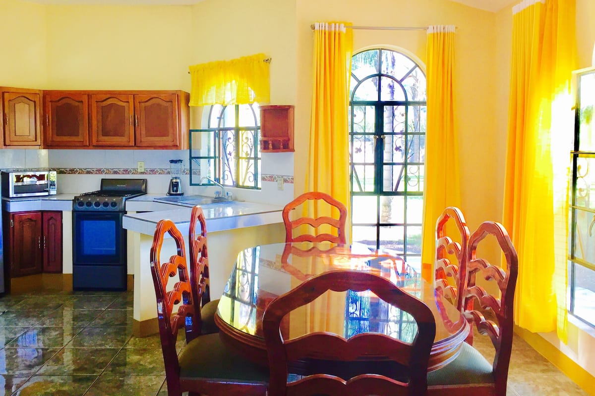 A kitchen with wooden cabinets, a stove, a sink, and a dining table with chairs.