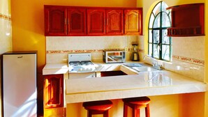 A kitchen with wooden cabinets, a microwave, a stove, and a refrigerator. - Guamúchil Parque Acuático & Cabañas (Etzatlan)