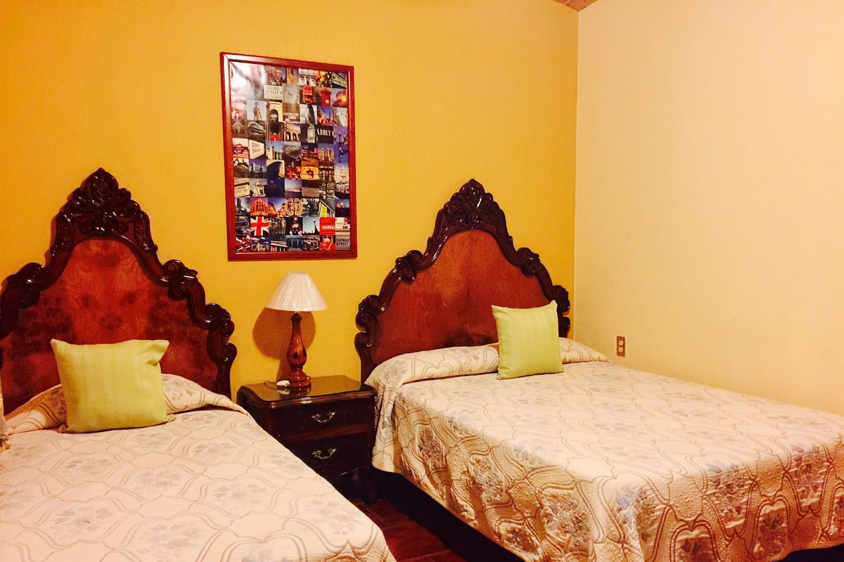 Two single beds with wooden headboards, a nightstand with a lamp, and a framed collage on the wall.