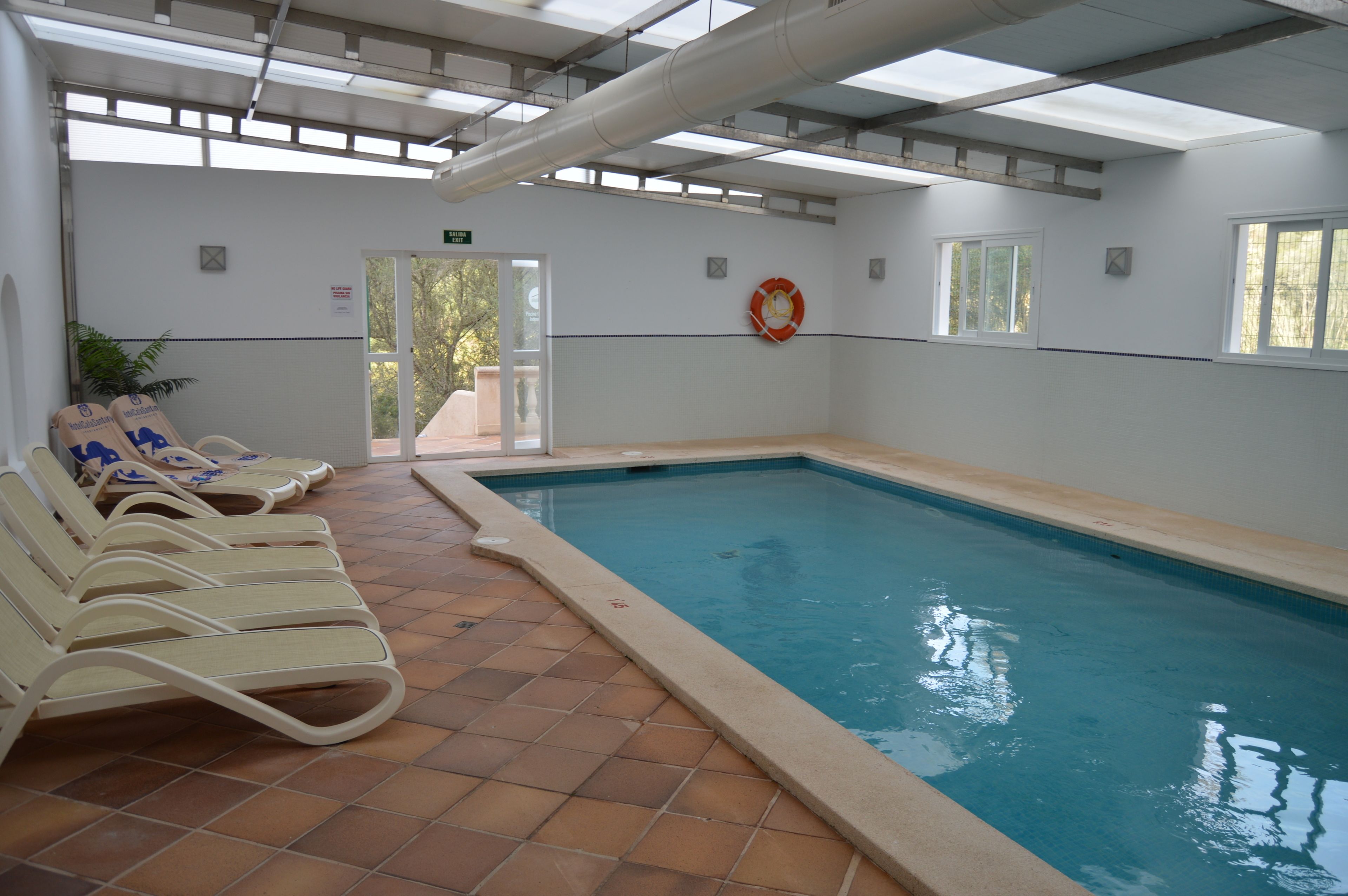 An indoor swimming pool with tiled flooring, lounge chairs, and a lifebuoy on the wall.