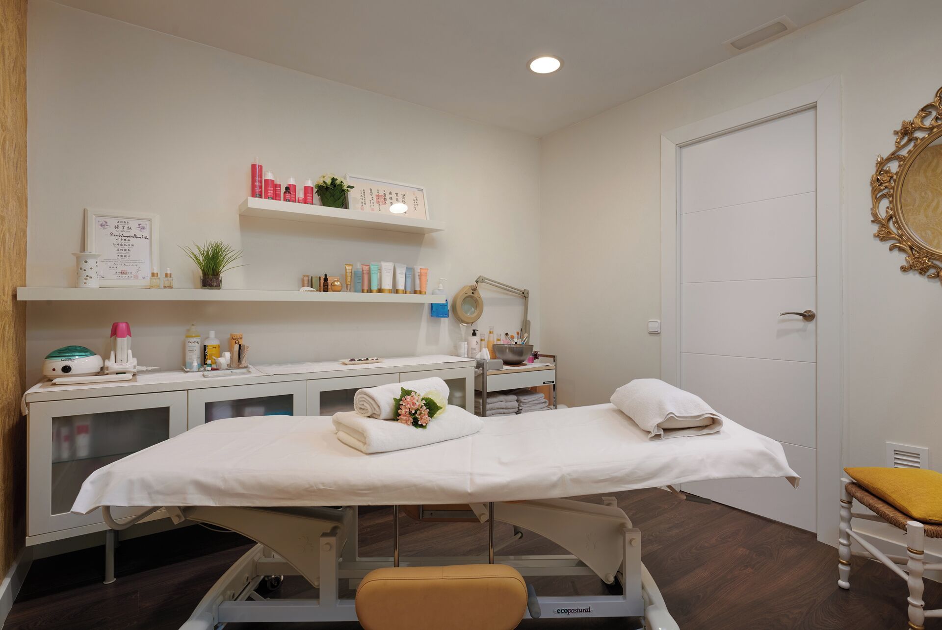 A clinical examination room with a treatment bed, medical equipment, and shelves with various products.