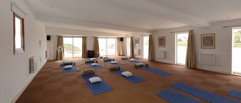 Amplia habitación con ventanas grandes, colchonetas de ejercicio y accesorios de yoga dispuestos para una clase de fitness.