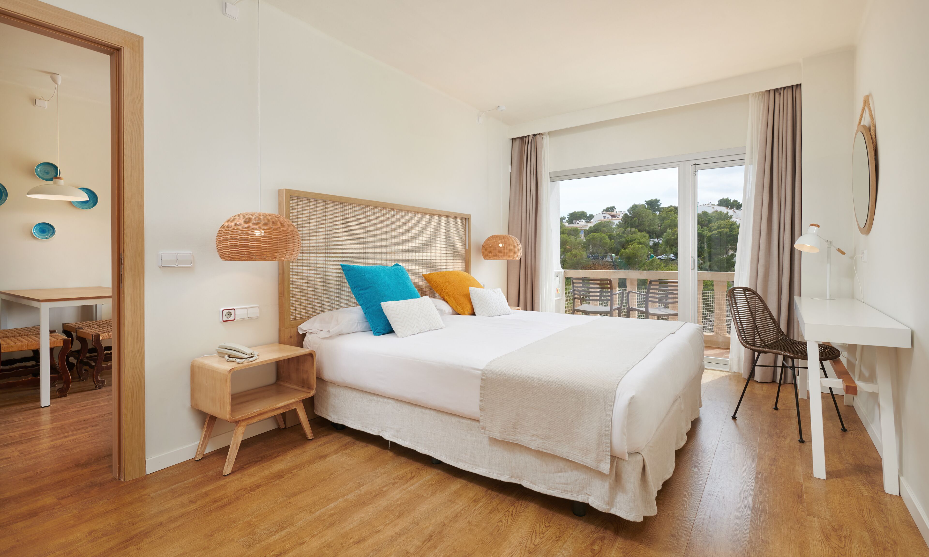 A modern hotel room with a large bed, a desk, and a balcony with outdoor seating.
