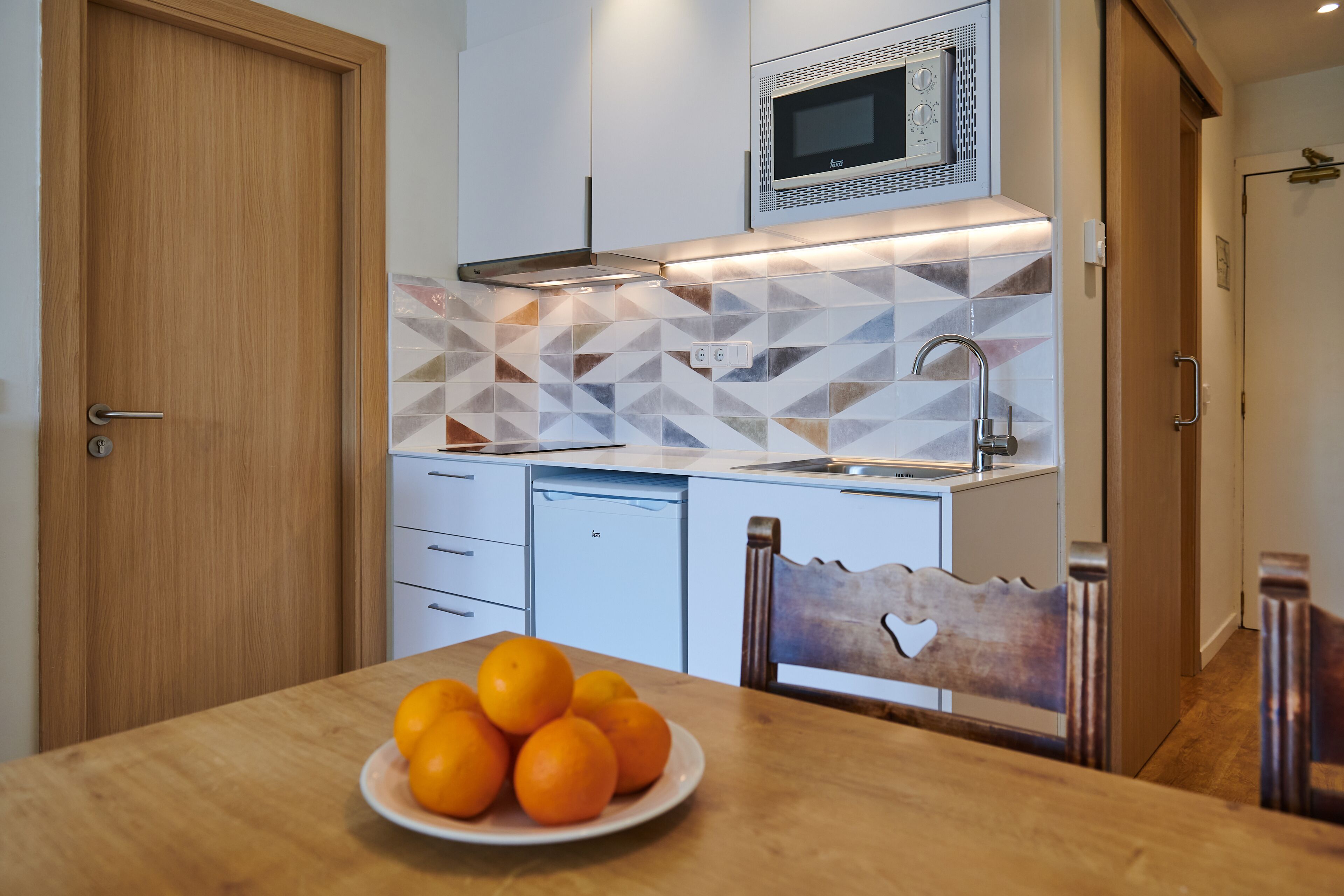 A modern kitchen with a microwave, a sink, and a plate of oranges on the table.