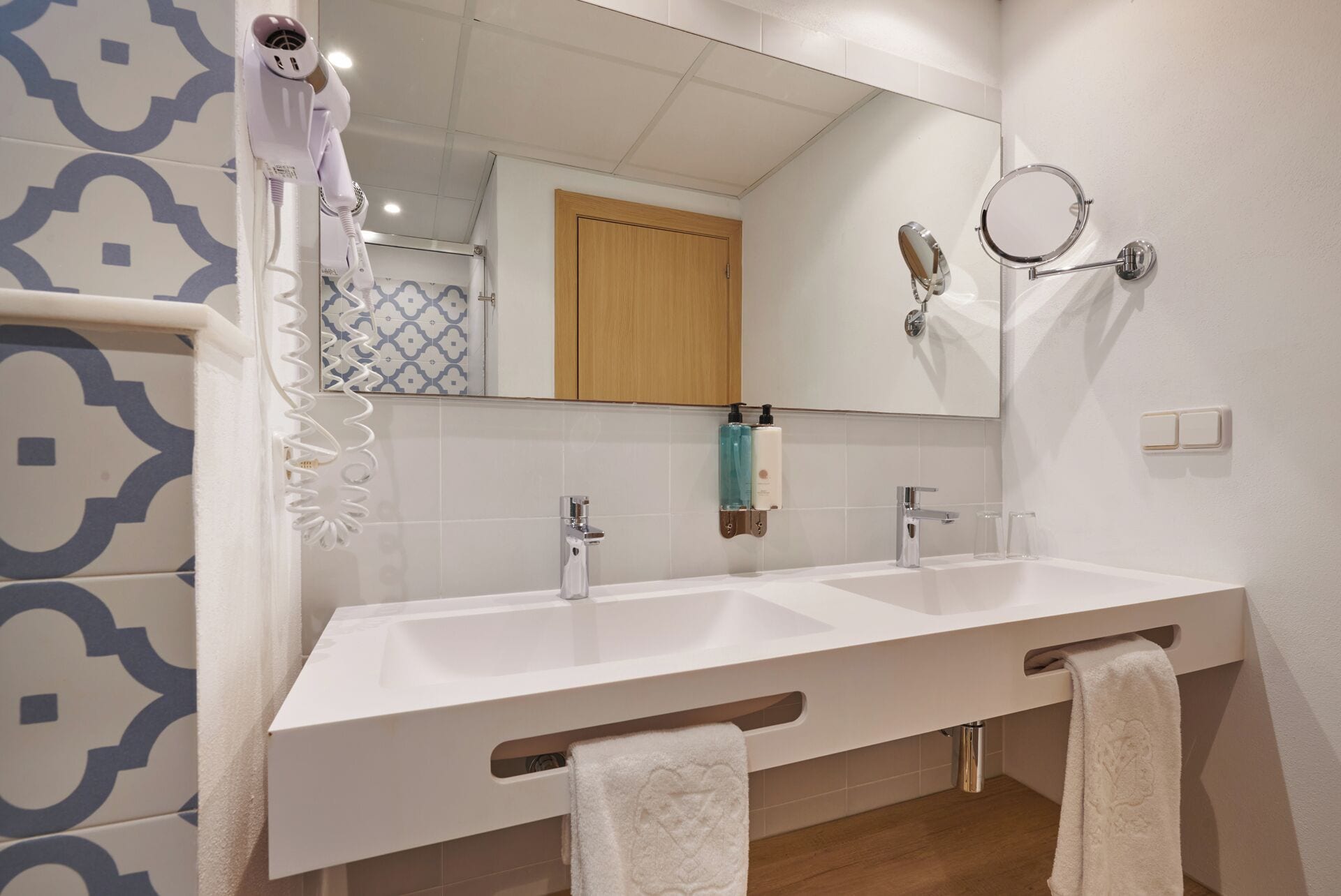 Uma casa de banho moderna com duas bacias, um secador de cabelo, um espelho com espelho redondo e um porta-toalhas.