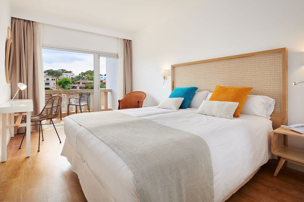 A hotel room with a large bed, a desk, a chair, a bedside table, and a view of the outside.