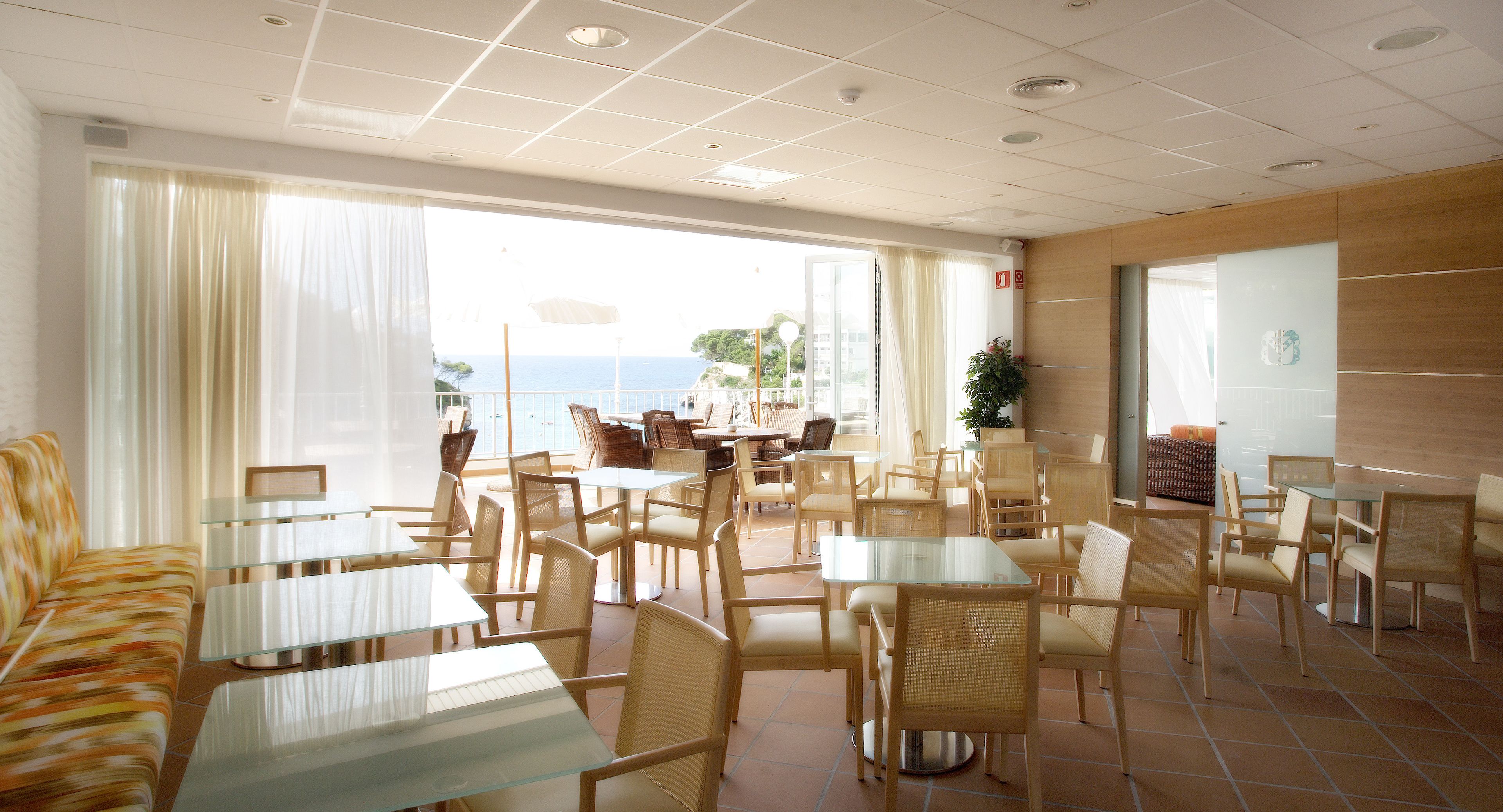 Un vestíbulo de hotel con varias zonas de estar, incluidas mesas y sillas, y grandes ventanales que ofrecen vistas al exterior.