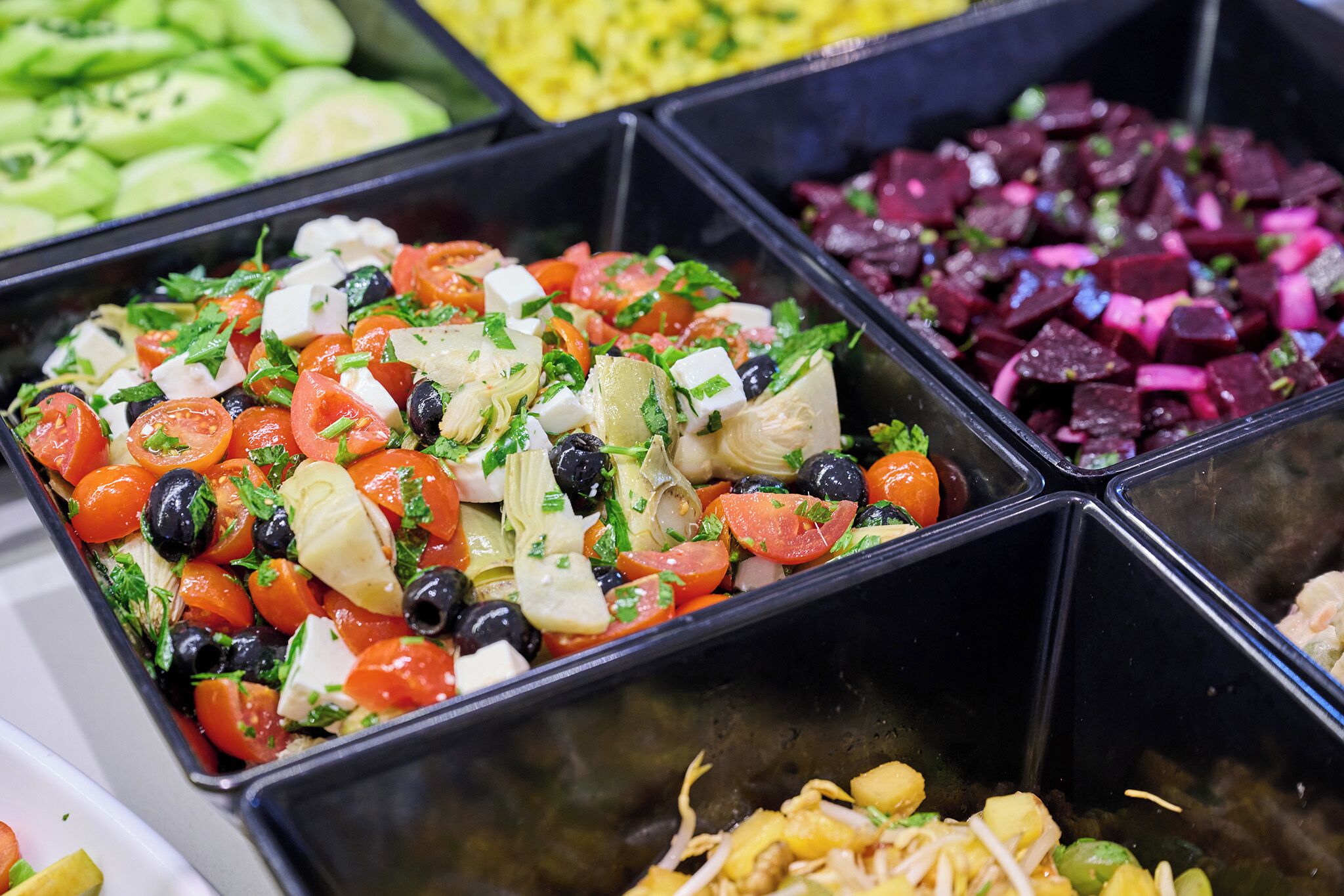A buffet with various salads including one with tomatoes, olives, and feta cheese.