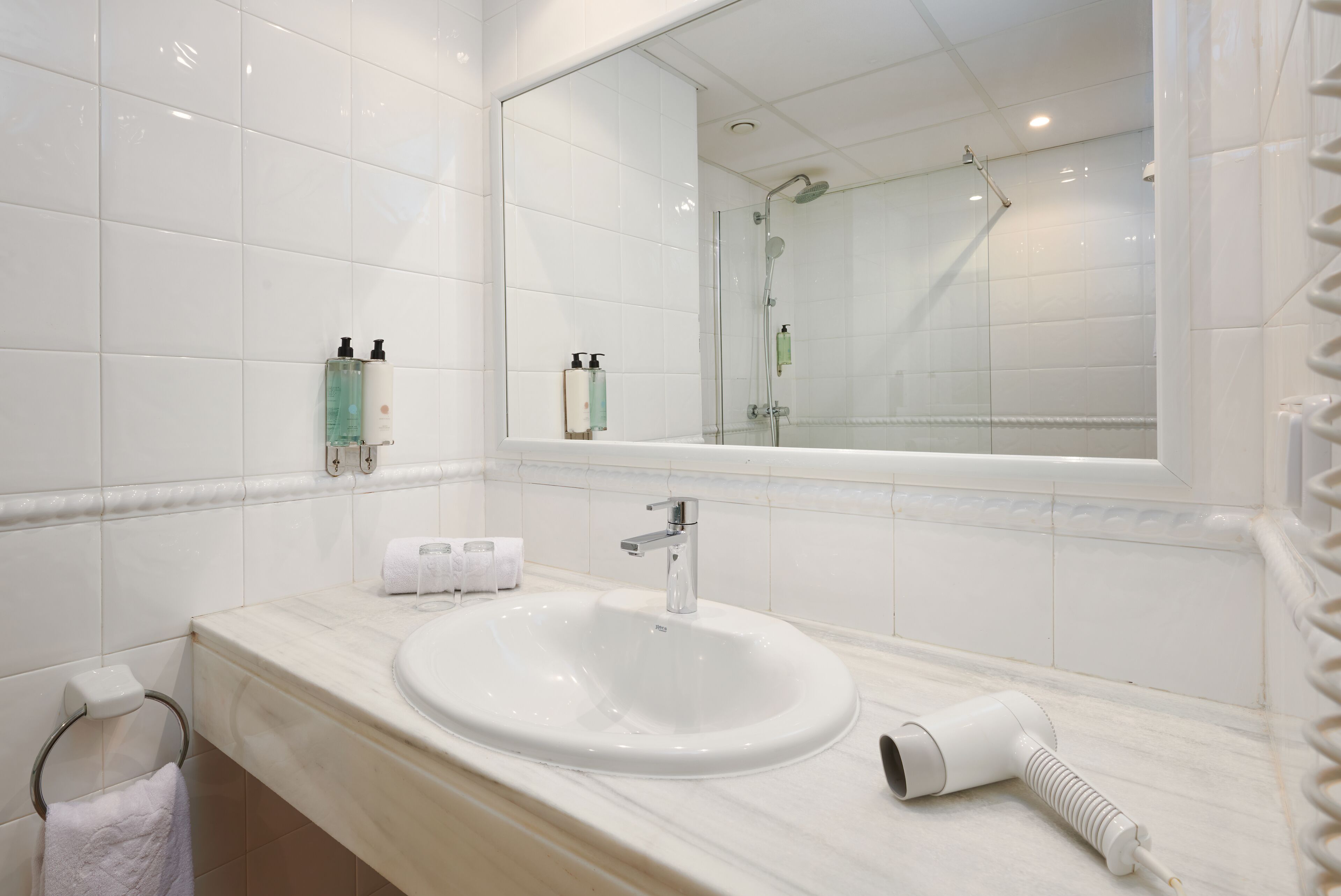 A modern bathroom with a white sink, a large mirror, and a glass-enclosed shower.