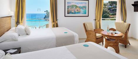 A hotel room with two beds, a dining table with chairs, and large windows with curtains.