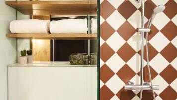 A bathroom with a glass shower enclosure, a wooden shelf with towels, and a potted plant.