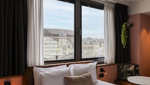 Habitación de hotel con cama, una mesita, una planta colgante y vistas a edificios históricos.