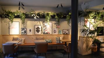 A cozy seating area with a bench and chairs, surrounded by framed artwork and lush green plants.