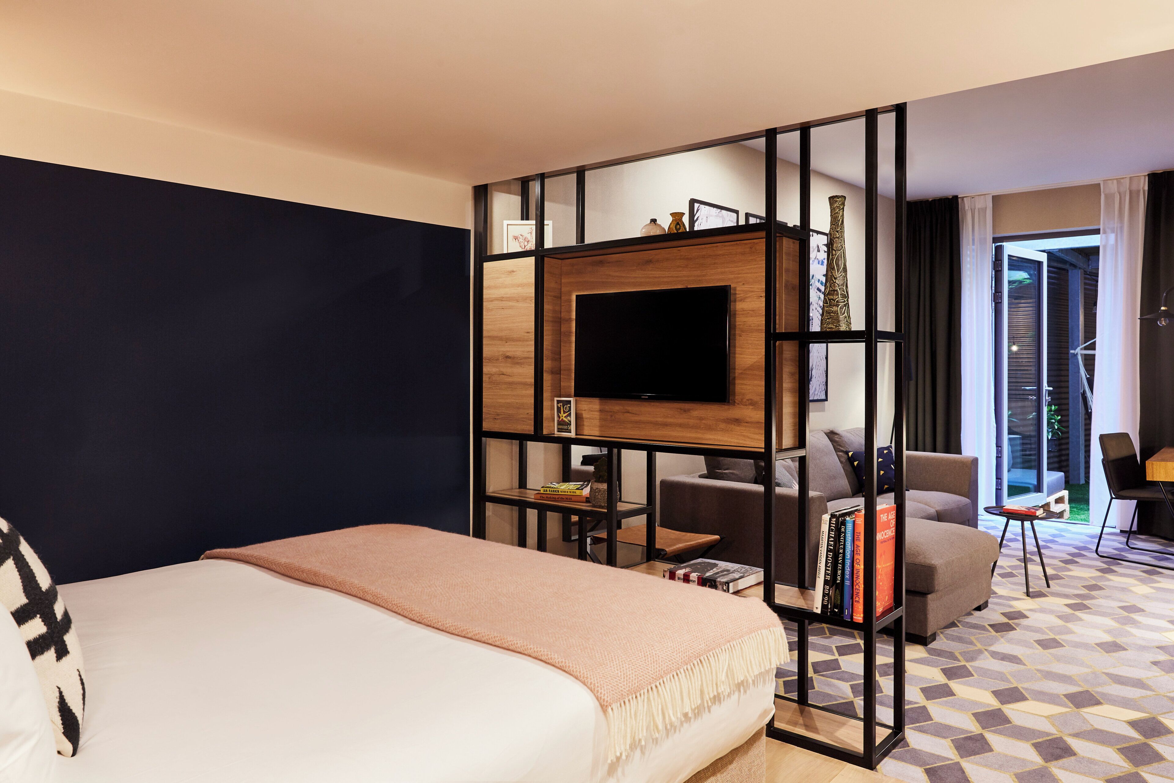 A hotel room with a bed, a TV, a seating area with a table, and a view of the outdoors.