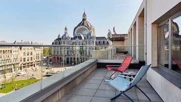 Een balkon met twee loungestoelen, een helder uitzicht op een historisch gebouw met koepels, en een tram op de achtergrond.