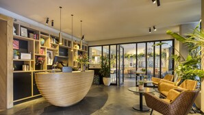 Un espace d’accueil moderne, avec un comptoir en bois, une grande plante en pot et un coin salon doté de fauteuils en cuir.