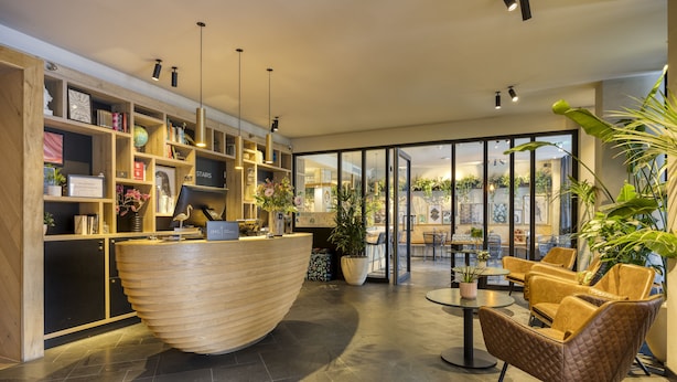 Una moderna zona de recepción con un mostrador de madera, una planta grande en maceta y un área de estar con sillones de cuero.
