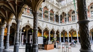 Un interior ornamentado con techos altos, columnas arqueadas y una zona central de estar con mesas y sillas.