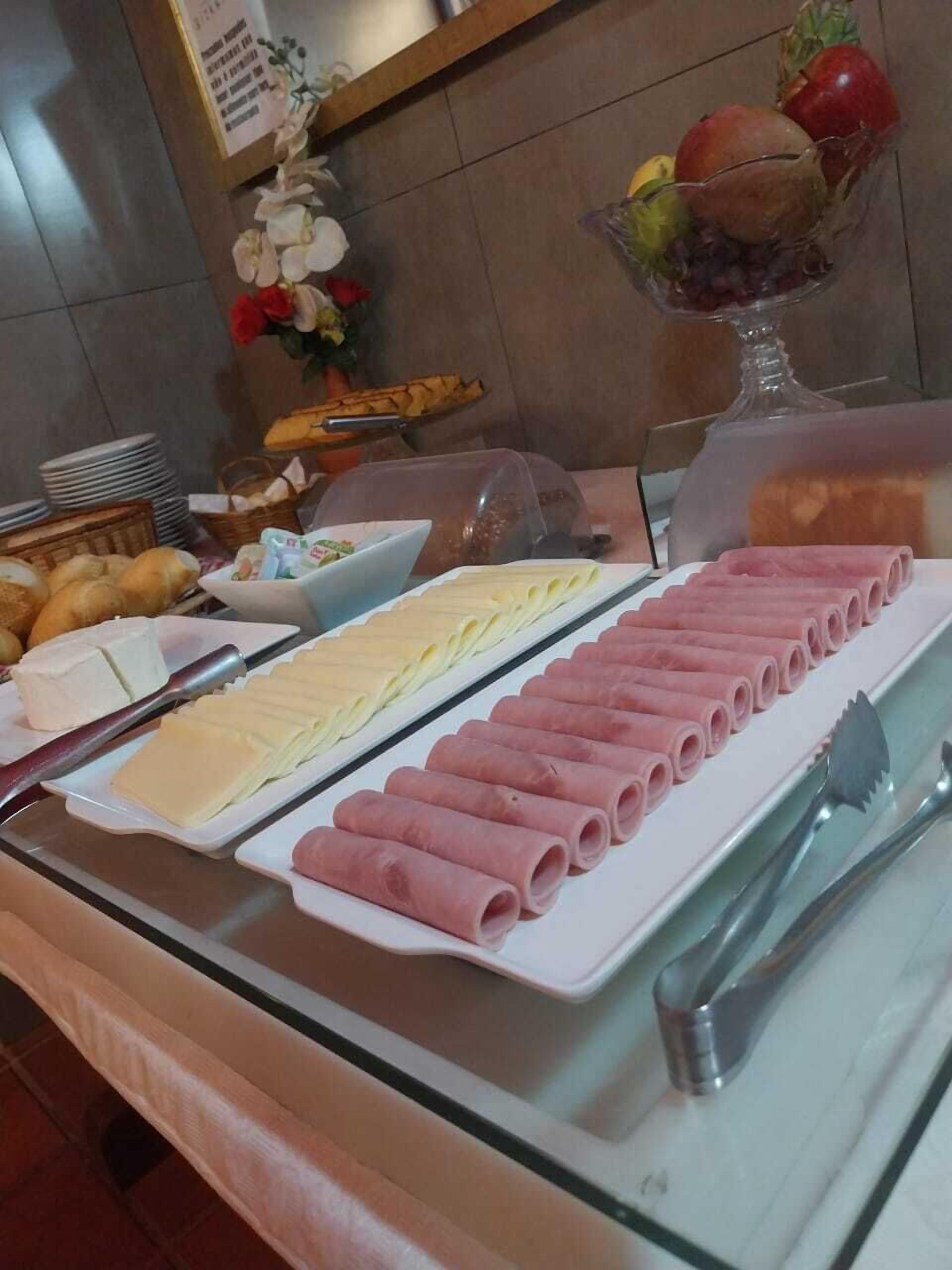 Una mesa de buffet con diversos alimentos, incluyendo queso en rodajas, jamón y un bol de fruta.