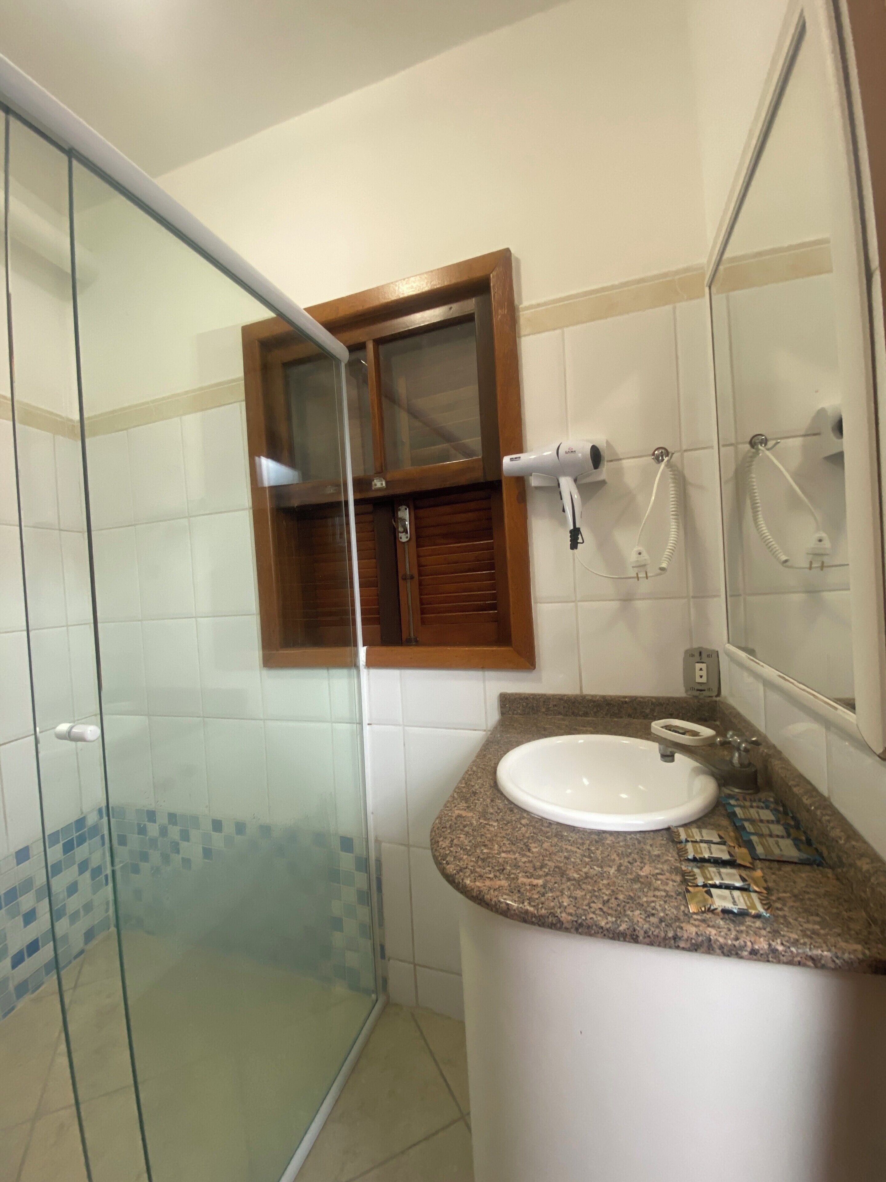 Un baño con cabina de ducha de vidrio, un lavabo con encimera de granito y un espejo sobre el lavabo.