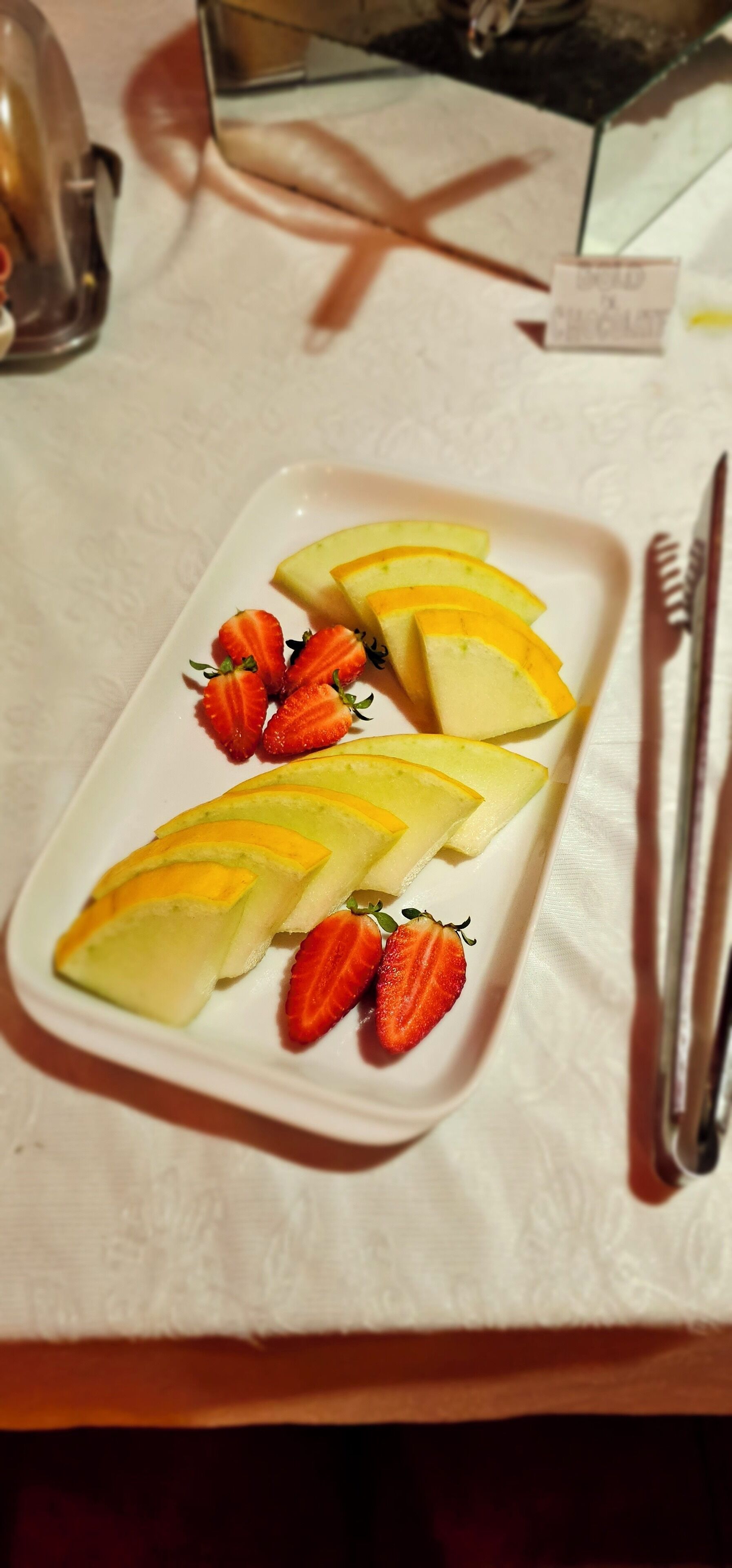 Plato blanco rectangular con rodajas de fruta amarilla y fresas sobre un mantel.