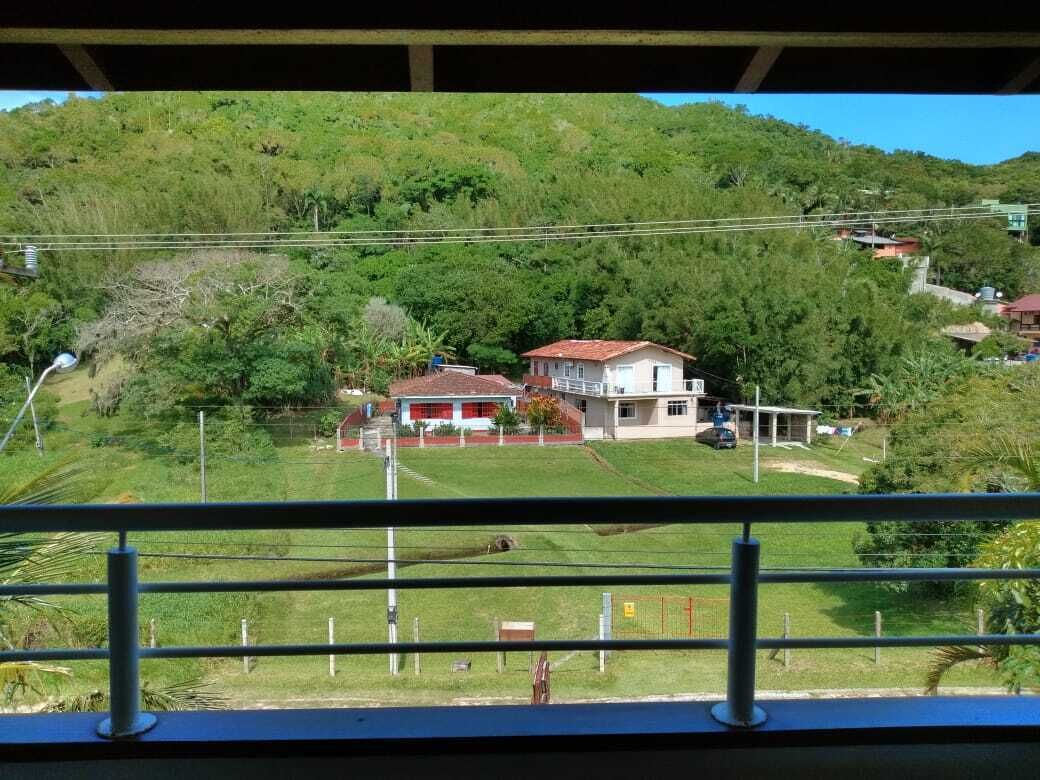 A house with a red roof and white walls, surrounded by lush greenery and hills.