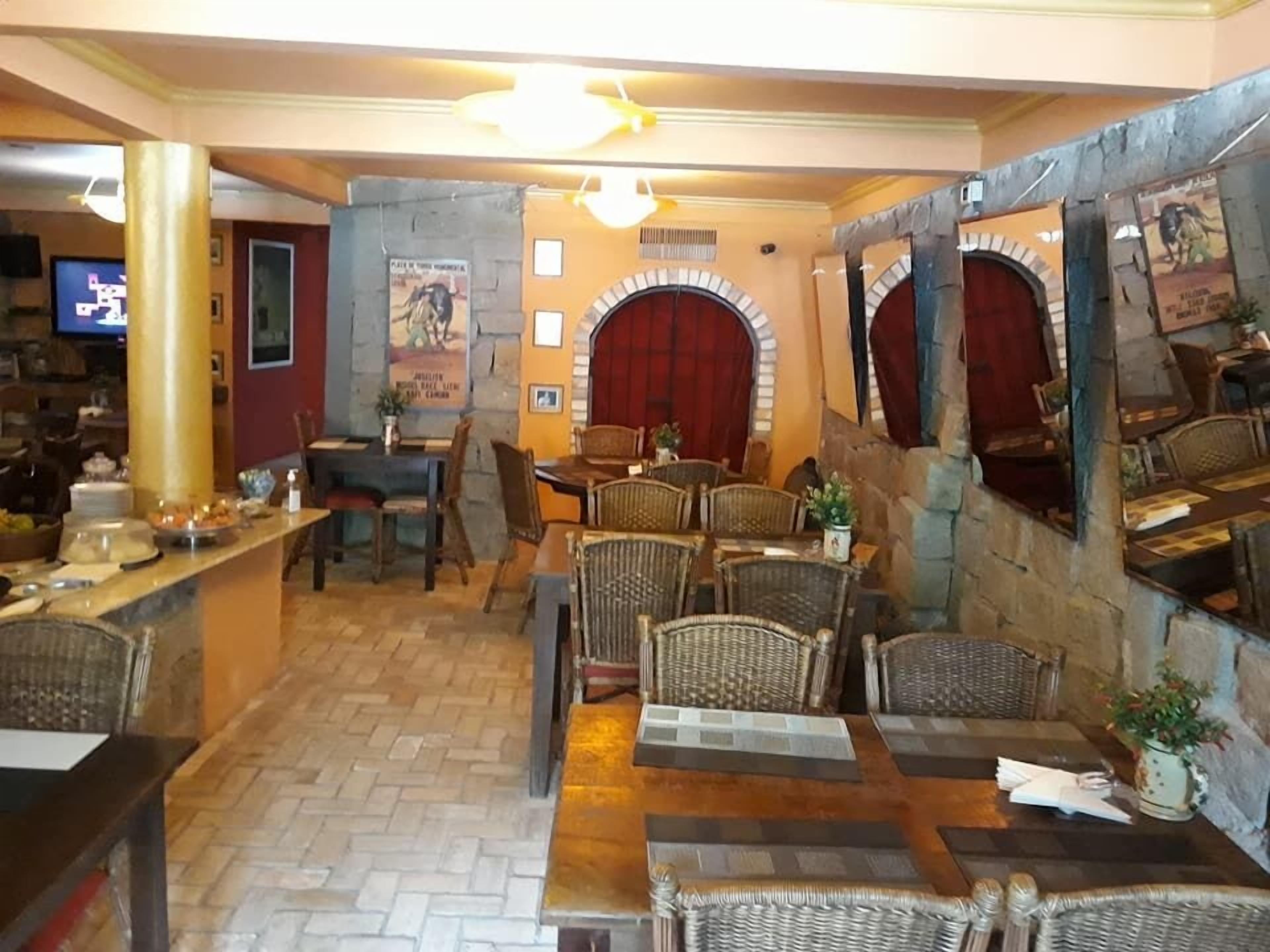 A restaurant with brick walls, wooden tables, wicker chairs, and a TV in the background.