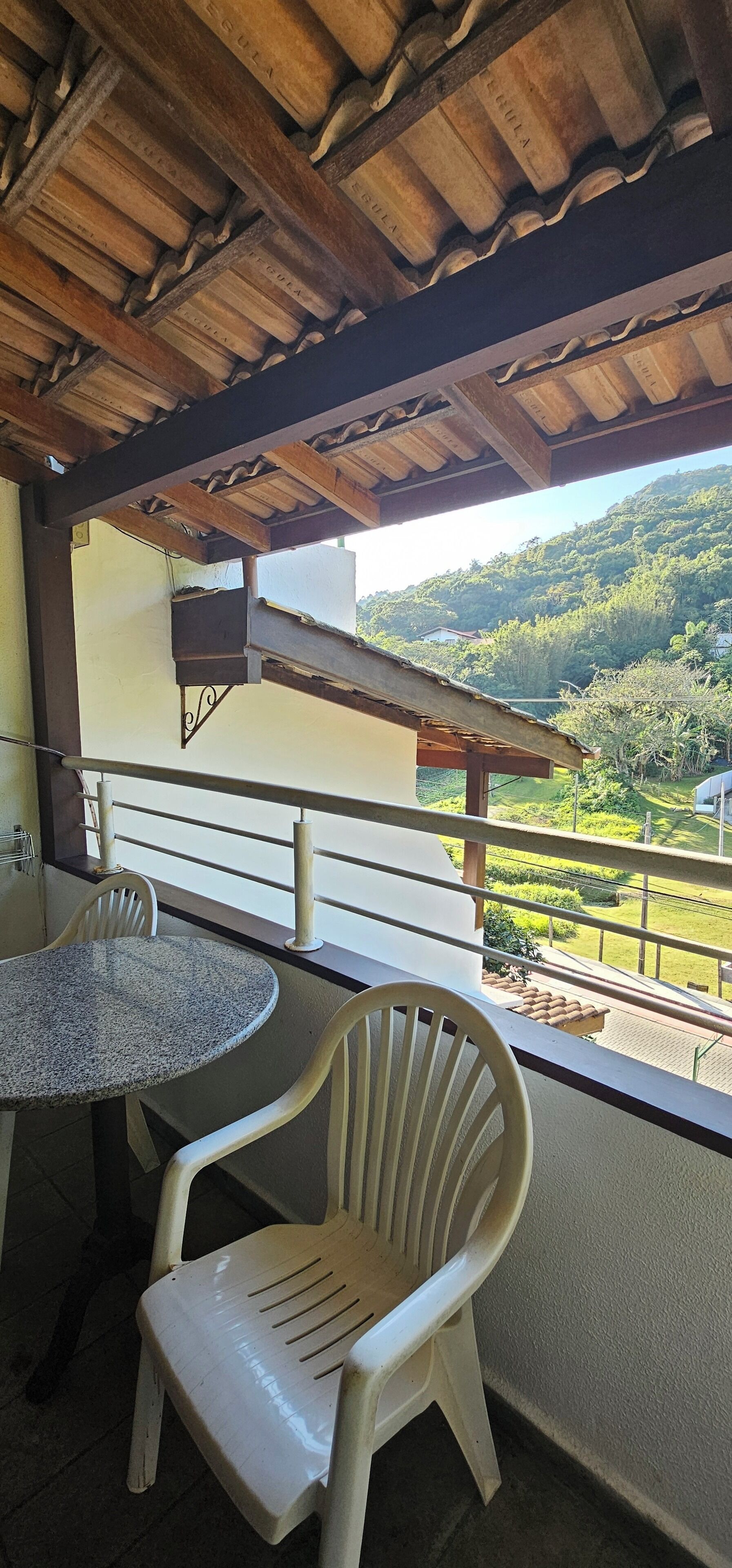 A balcony with a table and chairs, overlooking a green landscape with hills.