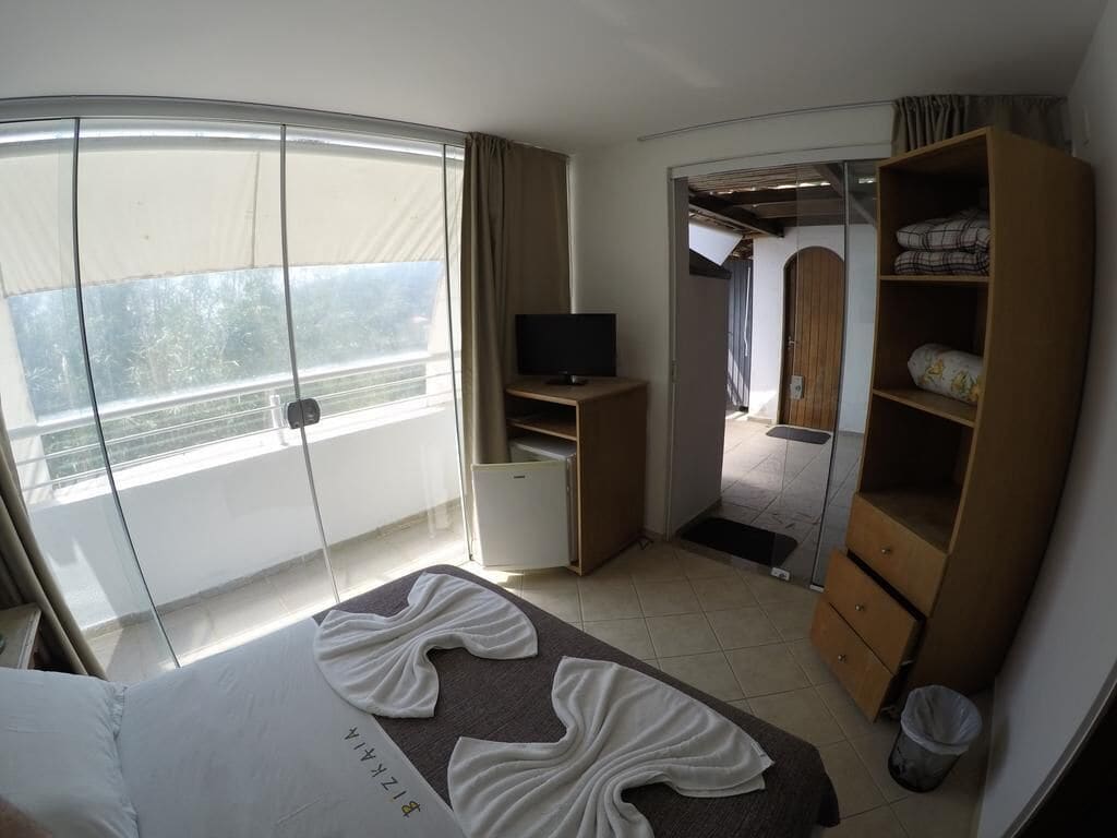A hotel room with a bed, a TV, a wardrobe, and a balcony with a view.