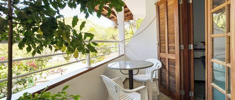 Een balkon met een tafel en stoelen, uitzicht op groen en een houten deur.