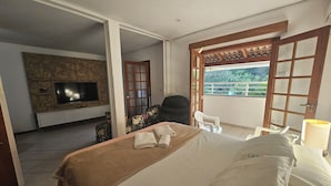 Habitación de hotel con cama, televisión, balcón con vistas y puerta de madera.