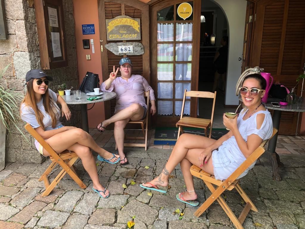 Three people seated at a table outside a building with a sign reading "RECEPTION TOQUE A CAMINHADA" and a number "682".